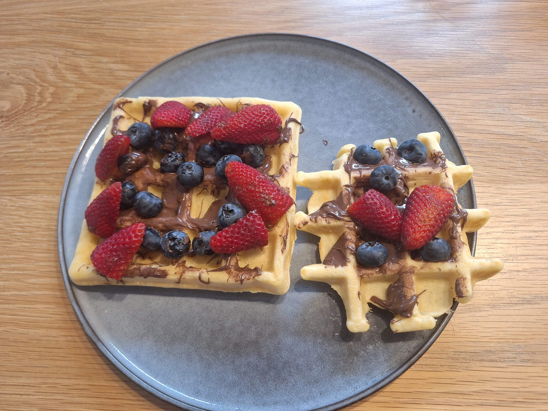 Two waffles topped with strawberries, blueberries and a drizzle of Nutella
